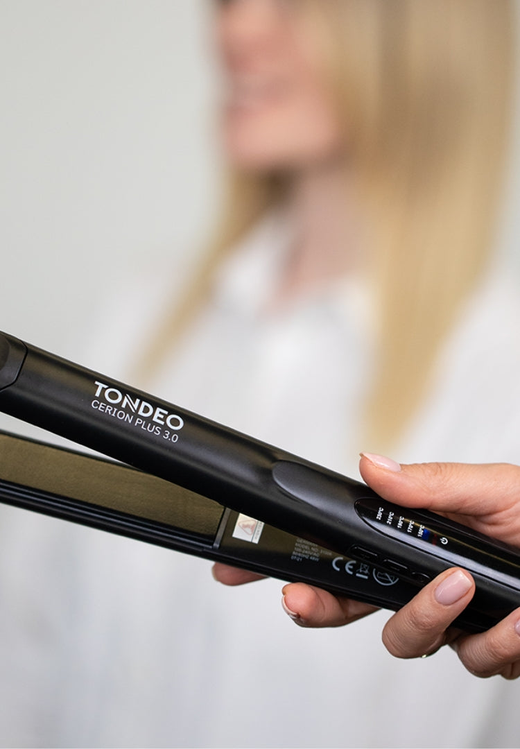 Peluquero sosteniendo una plancha alisadora, fondo desenfocado.