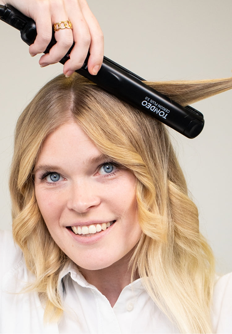Mujer peina el cabello con una plancha alisadora.
