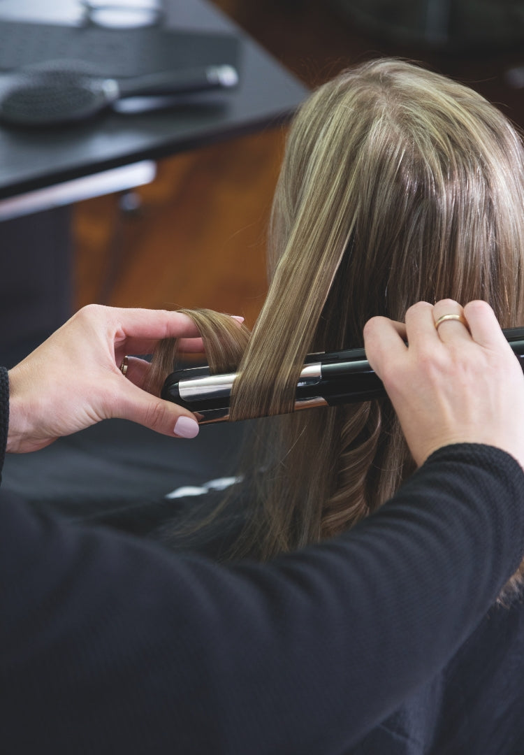 Il parrucchiere acconcia i capelli con la piastra